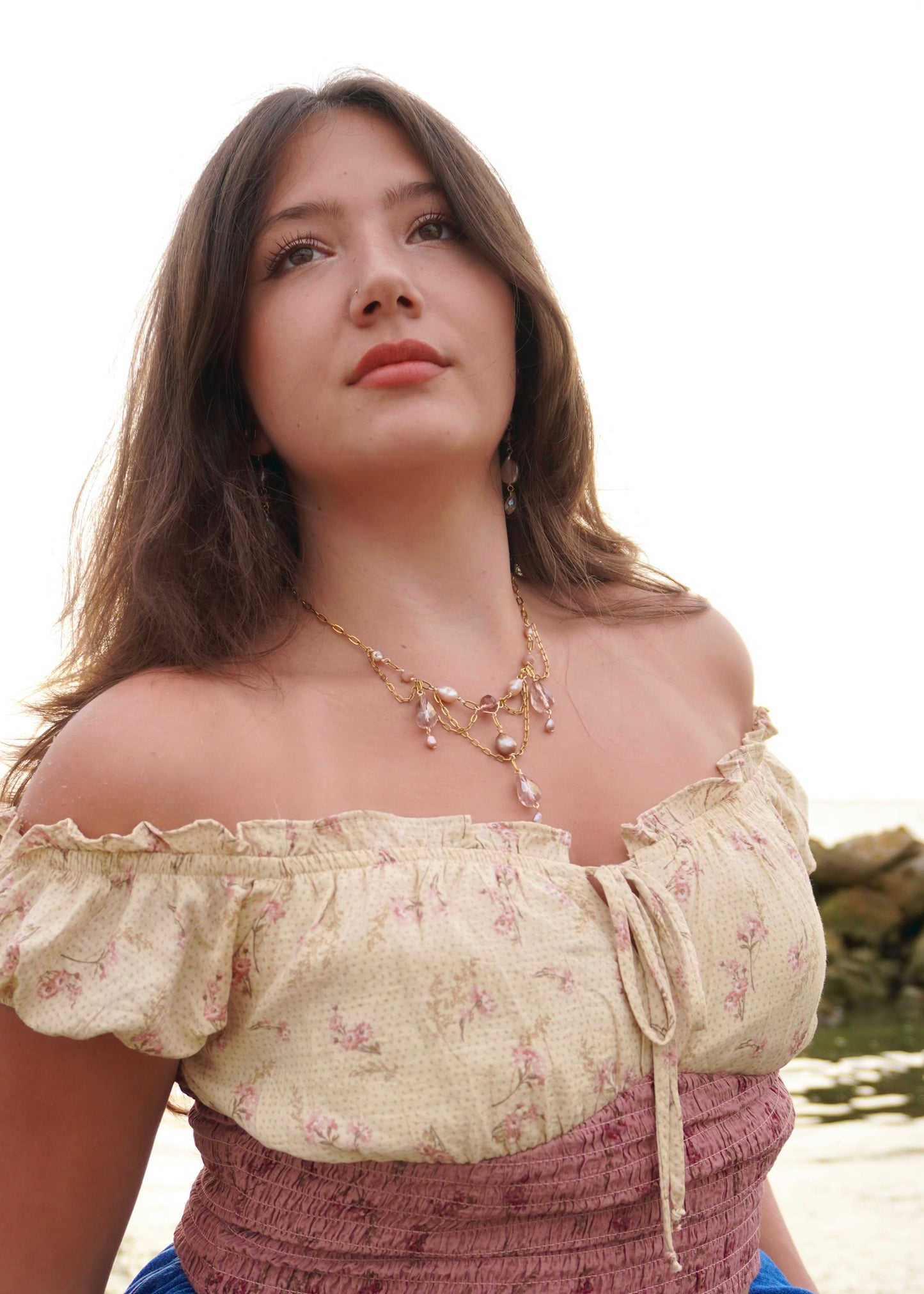 Woman wearing a floral off-shoulder top with a necklace, standing outdoors.
