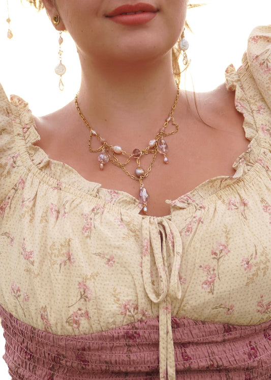 Close-up of a person wearing a floral dress and gold necklace with pink and purple pearl beads.